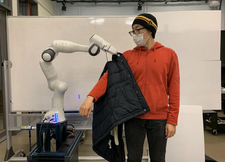 The robot helps to put a jacket on a human.