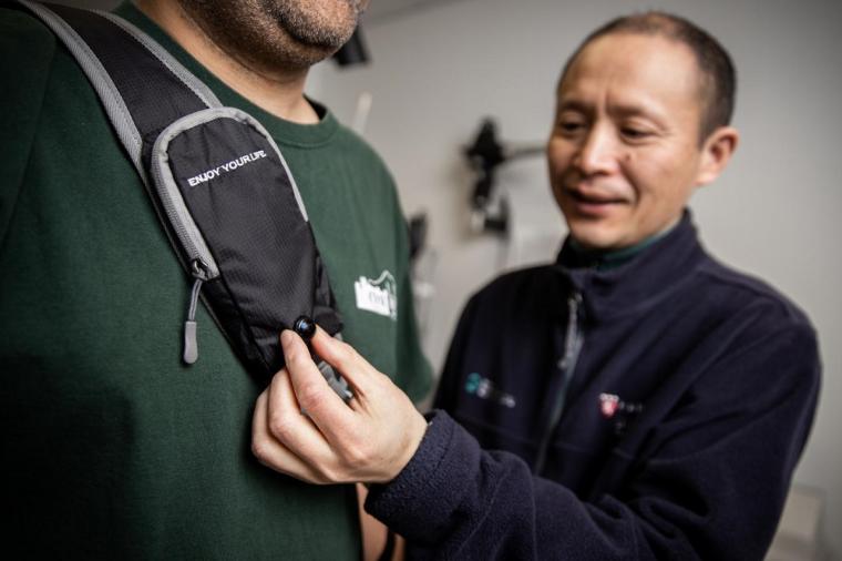 Gang Luo displays the camera on the strap of the wearable collision device.